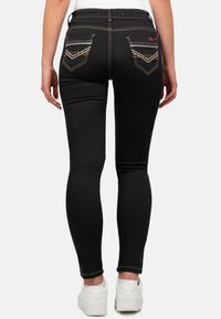 Zwarte jeans met een slim fit, voorzien van contrasterende gouden stiksels en een kenmerkend pocketontwerp aan de achterkant. G gedragen met witte schoenen.