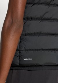 Vesta puffer neagră cu textură matlasată, având un logo WARMCELL. Materialul neted și tivul ribbat subliniază designul.
