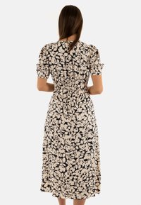 Abito con stampa floreale in crema e nero, caratterizzato da maniche a sbuffo corte, una vita arricciata e una lunghezza sotto il ginocchio. Tessuto morbido con un design fluido.