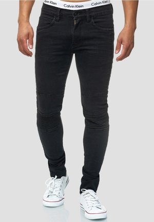 Jean skinny noir avec des panneaux côtelés aux genoux, zip à l'avant, poches avant et une ceinture avec le logo Calvin Klein blanc. Associé à des baskets blanches.