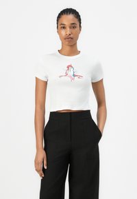 T-shirt blanc court avec un design de personnage imprimé en rose et bleu. Associé à un pantalon noir taille haute.