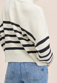 White knit sweater with navy stripes, featuring a loose fit, high collar, and ribbed cuffs, paired with light blue denim jeans.