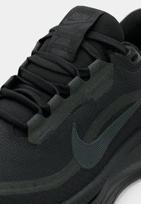 Dettaglio ravvicinato di una scarpa da corsa nera Nike con etichetta Gore-Tex, parte superiore in sintetico testurizzato e suola spessa e imbottita.