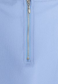 Světlá modrá zipová bunda vyrobená z látky s texturovaným povrchem. Zip je stříbrný s odpovídajícím světlým modrým poutkem.