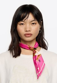 Silk scarf in vibrant pink with a decorative pattern featuring animals, tied around the neck with a contrasting accent at the knot.
