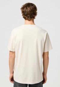 Lyhyt hihais beige t-paita, joka on valmistettu pehmeästä kankaasta. Paitaa koristaa pyöreä kaula-aukko ja rento leikkaus, eikä siinä ole näkyvää brändäystä tai kuvioita.