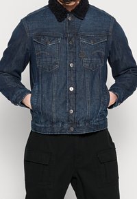 Jeansjacka i mörkblått med en strukturerad svart fårskinnskrage, med knappade framfickor och en figursydd design.