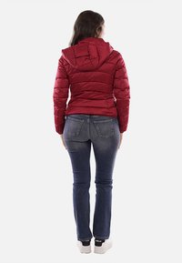 Giacca imbottita rossa con cappuccio, caratterizzata da un design trapuntato e cuciture. Abbinata a jeans blu e sneakers bianche con accenti neri.