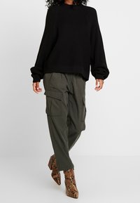 Pull noir en tricot avec un col rond, assorti d'un pantalon cargo vert olive avec poches latérales et des bottines à imprimé serpent marron.