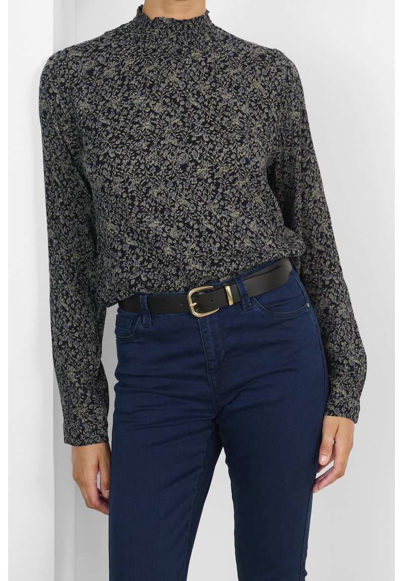 Bluzka z długim rękawem i wysokim kołnierzem w granatowym kolorze z kwiatowym wzorem w beżu i zieleni. Połączona z ciemnoniebieskimi dżinsami i czarnym paskiem.