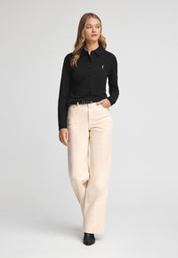 Camisa polo negra de manga larga con cuello y tapilla de botones, combinada con pantalones de pierna ancha en color crema y botines negros. Diseño sencillo.