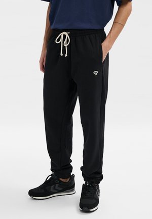 Sorte bomulds sweatpants med elastisk talje og justerbar cremefarvet snor, med sidelommer og et lille broderet logo.