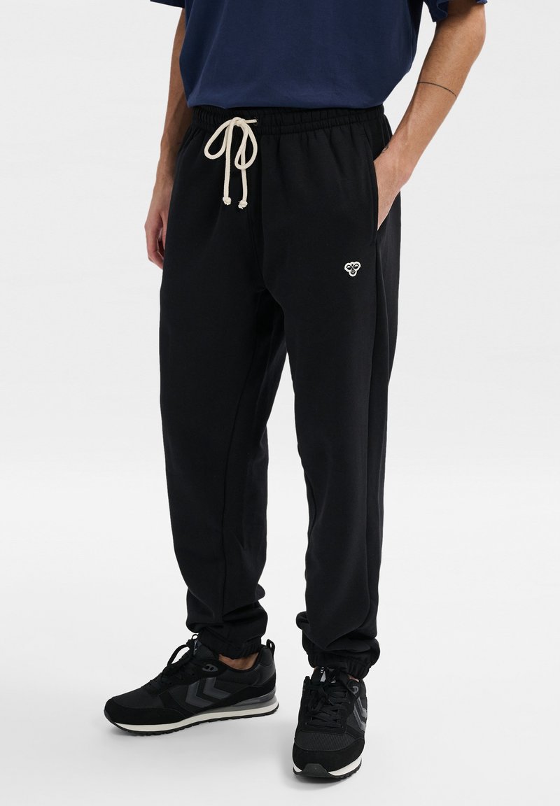 Schwarze Baumwoll-Sweatpants mit elastischem Bund und verstellbarem cremefarbenem Kordelzug, ausgestattet mit Seitentaschen und einem kleinen gestickten Logo.
