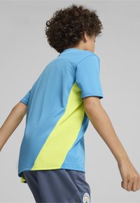 Lyhythihainen t-paita vaaleansinisellä sävyllä, jossa on neonkeltaiset vinopaneelit sivuilla. Paitalangassa on teksturoitu pinta ja klassinen kaulusrakenne.