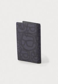 Tumehallist kangast rahakott, millel on abstraktne must muster, mis meenutab üksteise peale asetatud prille, seismas püstiselt heledal taustal.