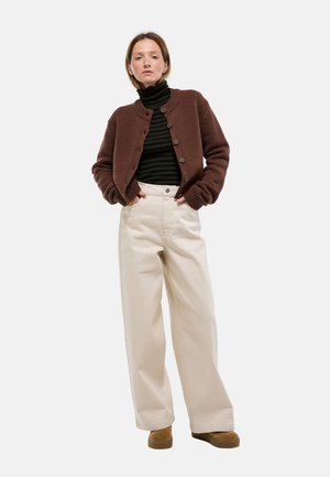 Cardigan brun en tricot avec des boutons, associé à un col roulé rayé noir et vert et un pantalon beige à jambes larges. Chaussures marron visibles.