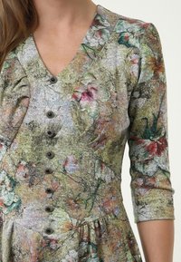 Kleid mit Blumenmuster aus strukturiertem Stoff in Grün-, Rosa- und Beigetönen. Verfügt über einen V-Ausschnitt, Puffärmel und schwarze Knöpfe auf der Vorderseite.