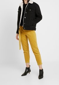 Svart denimjacka med krämfärgad fuskpälskrage, kombinerad med senapsgula kordbyxor. Svarta ankelstövlar med spetsiga tår och kitten heels.