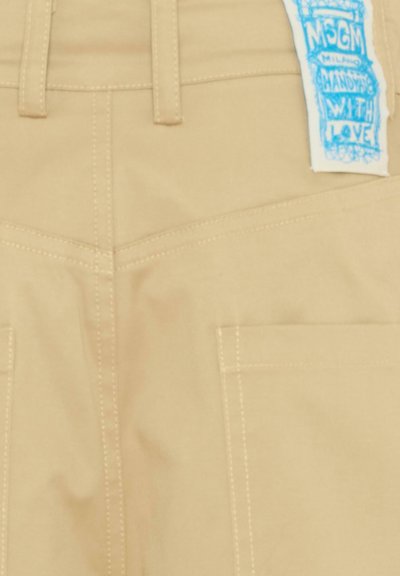 Poche arrière d'un pantalon beige avec des passants de ceinture et une étiquette de marque MSGM Milano bleue cousue sur la ceinture.