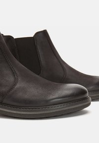Cizme negre din piele până la gleznă, cu panouri laterale elastice, vârf rotunjit și finisaj texturat. Talpa este gri cu un model de profil discret.