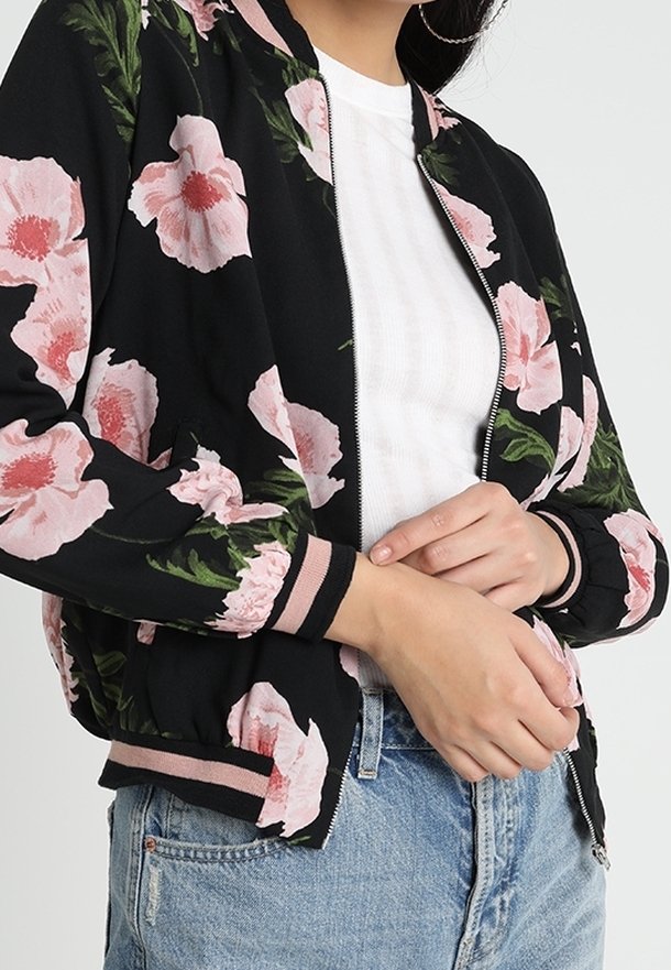 Giacca bomber nera con grandi motivi floreali rosa, polsini e vita a costine; presenta una chiusura con zip sul davanti e un tessuto leggero.