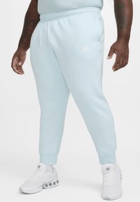 Pantalones de chándal Nike de color azul claro con cintura elástica, puños ajustados y un pequeño logo blanco. Llevados con zapatillas deportivas blancas.