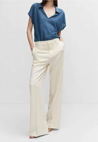 Modrá polo košile s krátkým rukávem v kombinaci s širokými béžovými kalhotami. Kalhoty mají boční kapsy a hladkou texturu látky.