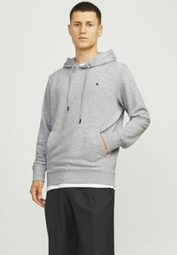 Grauer Hoodie mit Kordeln, Fronttasche und gerippten Bündchen. Mit kleinem schwarzem Logo und geschichtetem Saum über schwarzen Hosen.