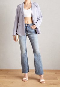 Jasnofioletowy blezer, biały krótki top i jasnoniebieskie rozkloszowane dżinsy. Białe sandały na obcasie. Materiał wydaje się gładki; subtelne przetarcia na dżinsach.