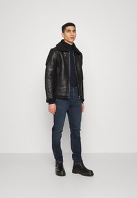 Casaco bomber de couro preto com colarinho de pele de carneiro, combinado com jeans escuros e botas de tornozelo pretas. Textura suave, design ajustado.