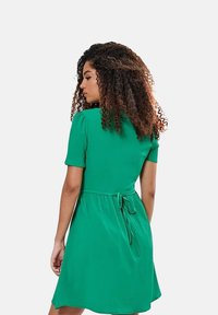 Groene jurk met korte mouwen en een strikontwerp aan de achterkant, met een getailleerde bovenkant en een uitlopende rok, gemaakt van een lichtgewicht, gladde stof.