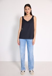 Granatowa bezrękawnikowa bluzka z dekoltem w serek i marszczonymi ramiączkami, zestawiona z jasnoniebieskimi prostymi dżinsami i czarno-białymi sneakersami.