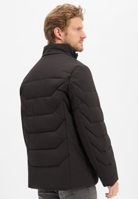 Czarna kurtka puchowa z wysokim kołnierzem, w wykonaniu z chevronowym pikowaniem i gładką teksturą. Projekt jest elegancki i dopasowany w okolicy ramion.