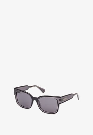 Mustat suorakulmion muotoiset aurinkolasit, joissa on tummat, sävytetyt linssit, paksut muovikehykset ja kapenevat sankat, joissa on kultaiset logoelementit.