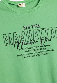 Zielona bawełniana koszulka z okrągłym dekoltem. Posiada odważny czarny tekst: "NOWY JORK MANHATTAN Numer Jeden" oraz inspirujące hasła poniżej.