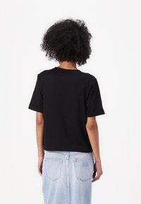 T-shirt nero a maniche corte con scollatura rotonda e maniche arrotolate, abbinato a una gonna di jeans azzurri con tasche posteriori.