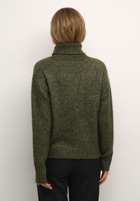 Pull en maille olive avec un col roulé haut, des poignets et un ourlet côtelés ; il présente un matériau doux et texturé avec une coupe décontractée.