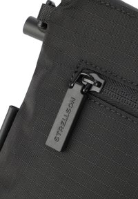 Borsa in nylon nero con superficie texturizzata, chiusura con zip e zip pull nero, e un'etichetta brandizzata con il logo "STRELLSON".
