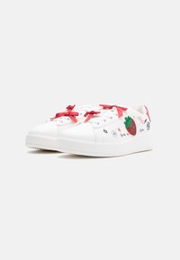 Baskets blanches à texture lisse, avec des lacets en satin rouge, une fraise brodée, et des griffonnages colorés sur les côtés. Semelle épaisse blanche.