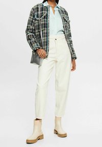 Vävd jacka i blå, grön och creamfärgade toner, ljusblå skjorta, creamfärgade byxor och beige ankle boots med kraftig sula, matchat med en silverfärgad väska.