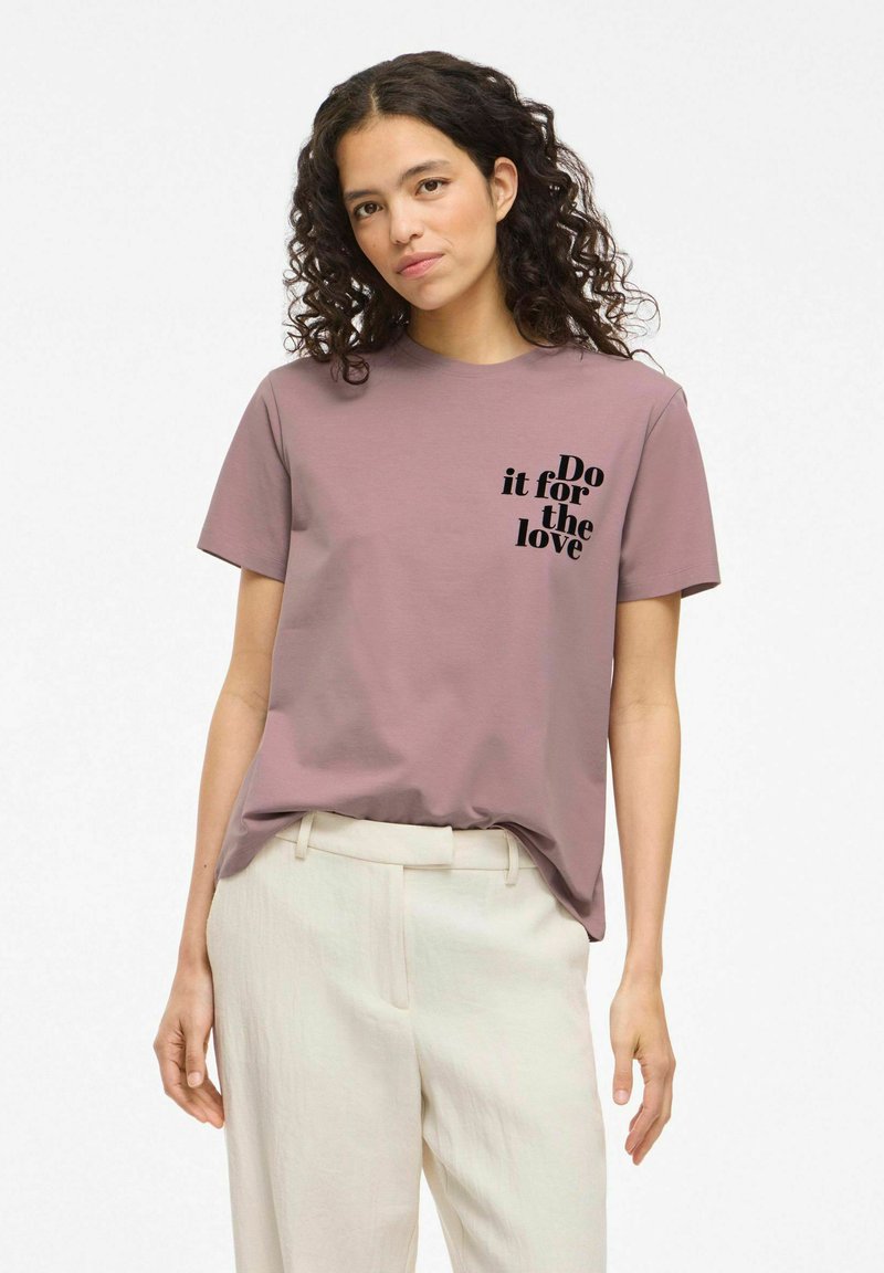 Camiseta de algodón de manga corta en color malva con cuello redondo, que presenta texto negro: "Hazlo por amor" en el lado izquierdo.