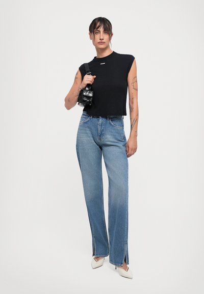 Black sleeveless top with a cropped design, paired with light blue denim jeans featuring split hems and white pointed-toe heels.