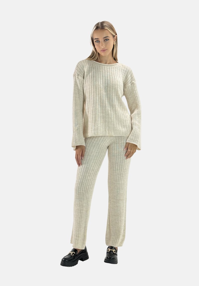 Kremowy sweter z prążkowanej dzianiny i pasujące spodnie o luźnym fasonie, z długimi rękawami i subtelnymi detalami. Uzupełnione czarnym obuwiem.