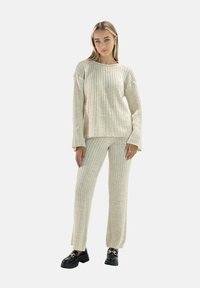 Beige ribbad tröja och matchande byxor, med långa ärmar och en avslappnad passform. Tyget verkar mjukt med en lätt texturerad yta.