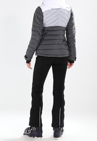 Grå puffjacka med en vit övre del och chevronmönster, ihopkopplad med svarta byxor med dragkedjor och skidstövlar med spännen.