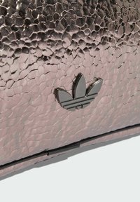 Metalik ružičasta torba s teksturom i crnim logotipom s tri pruge. Površina ima teksturu poput kovačkog udarca s vidljivom trodimenzionalnom kvalitetom.