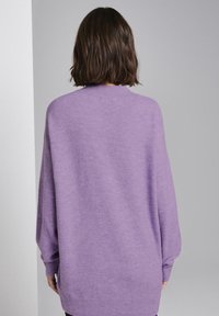 Pull violet oversize en tricot doux avec des manches longues et un col rond, présentant une coupe décontractée et des poignets côtelés.
