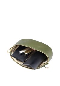 Petit sac vert zippé partiellement ouvert montrant deux rouges à lèvres, un portefeuille noir et un étui noir pour lunettes de soleil à l'intérieur.