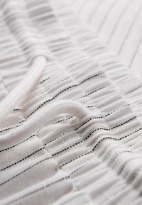 Gros plan d’un tissu blanc avec de fines rayures horizontales noires et un cordon blanc passé dans une ceinture élastiquée.