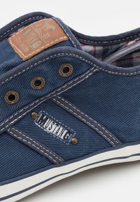 Modrá plátěná teniska s kontrastním prošíváním, kovovými průchody na tkaničky, károvanou výstelkou a koženou nášivkou s logem koně. Bílá gumová podrážka.